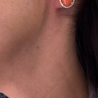 Arete ovalado tono coral con halo circular colocado en oreja
