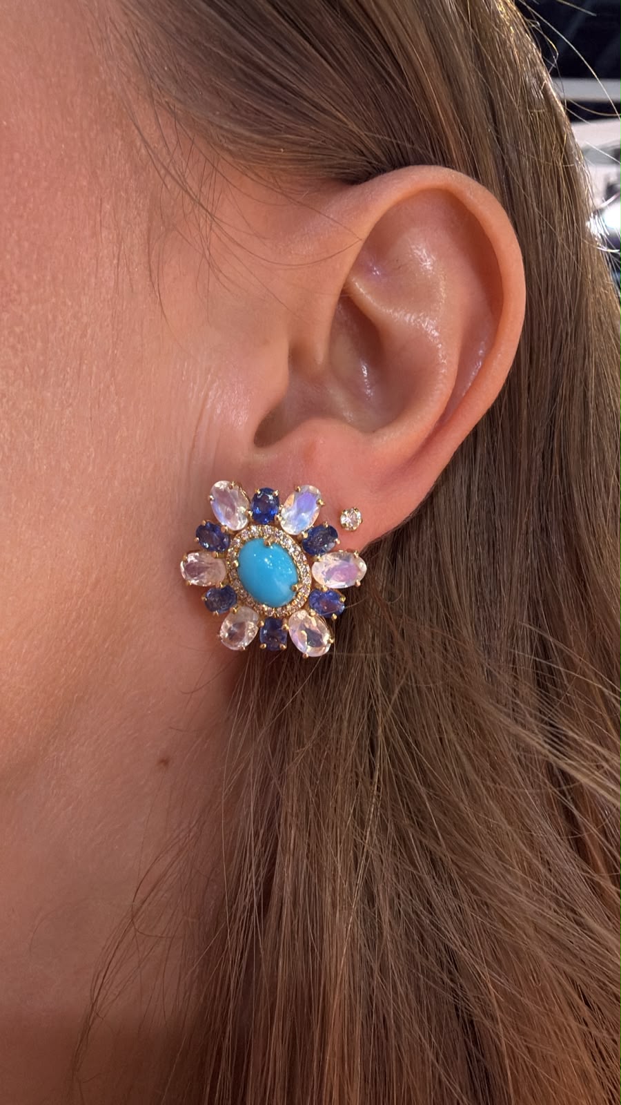 Arete floral con centro azul y piedras multicolor colocado en oreja
