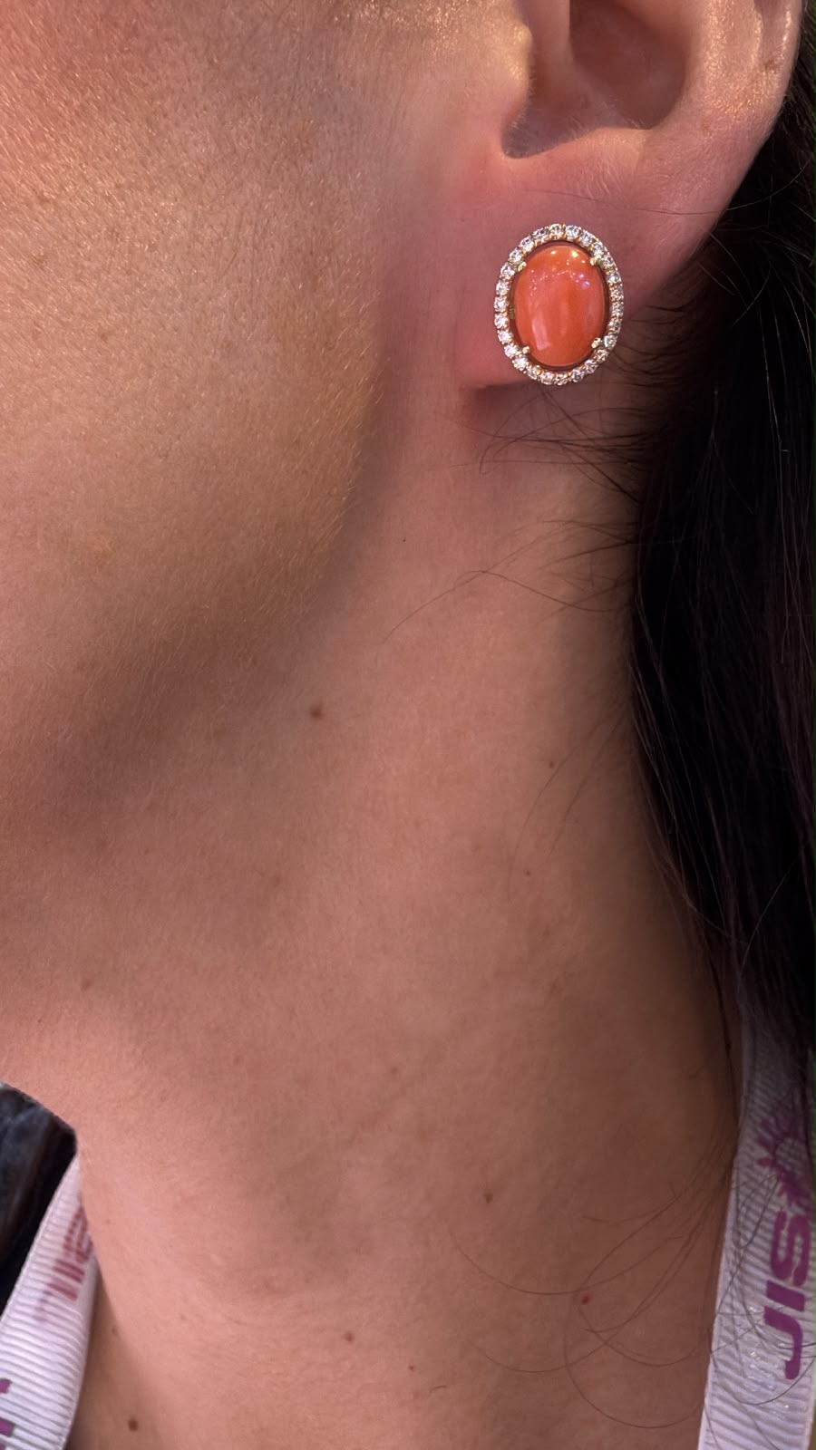 Arete ovalado tono coral con halo circular colocado en oreja